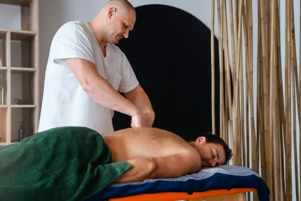 Terapeuta aplicando massagem nas costas de um homem deitado, promovendo relaxamento e alívio muscular