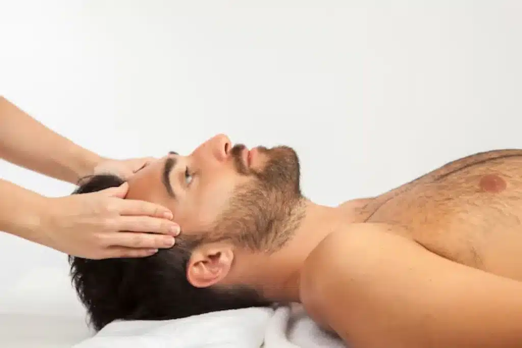 Homem deitado recebendo massagem na cabeça, representando um momento de relaxamento e bem-estar.