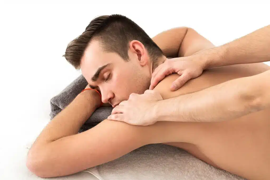 Homem deitado de bruços recebendo uma massagem tântrica nas costas, com as mãos do terapeuta aplicando pressão suave para relaxar e aliviar tensões musculares.