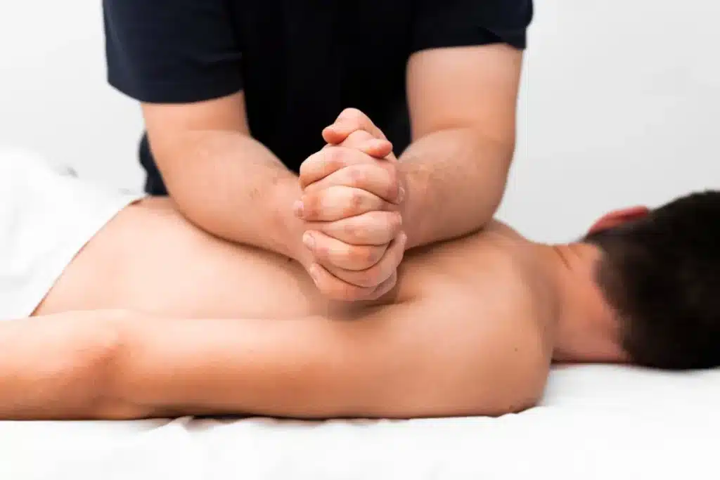 Profissional aplicando uma massagem terapêutica nas costas de um cliente, utilizando pressão com as mãos em um ambiente tranquilo