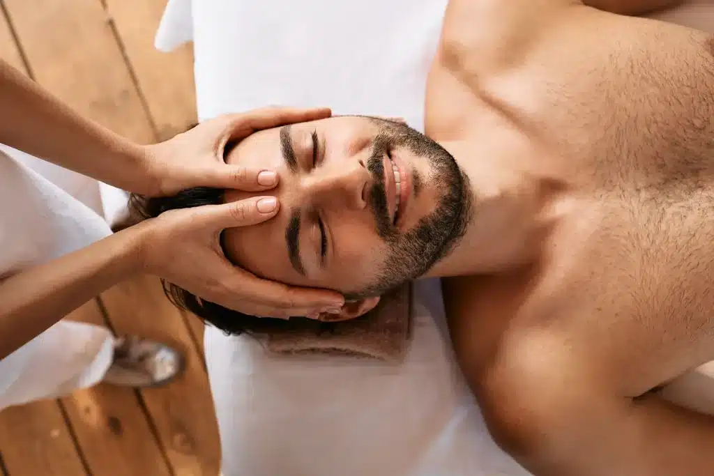 Homem relaxado recebendo massagem facial em ambiente tranquilo e aconchegante.