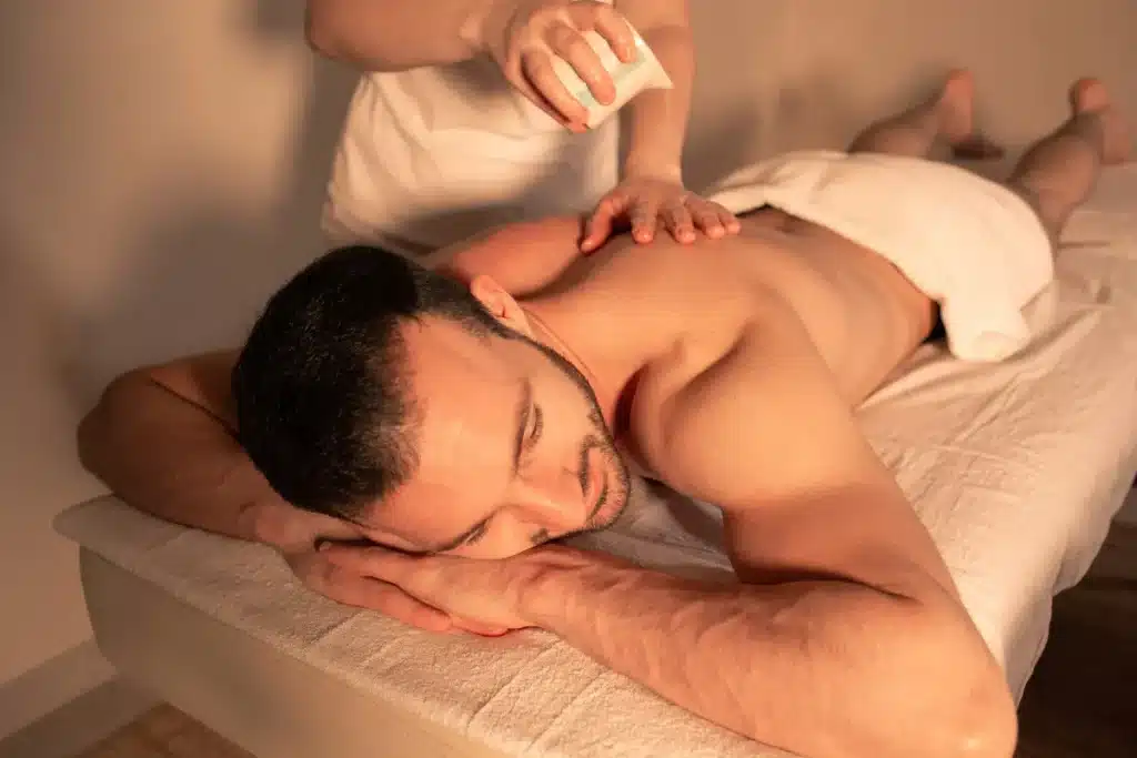 Homem recebendo massagem relaxante nas costas com óleo em ambiente acolhedor e iluminado com luz suave.