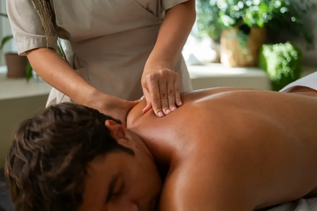 Massagista profissional realiza massagem terapêutica nas costas de um homem, focando no relaxamento muscular e alinhamento energético dos chakras em um ambiente tranquilo e natural.