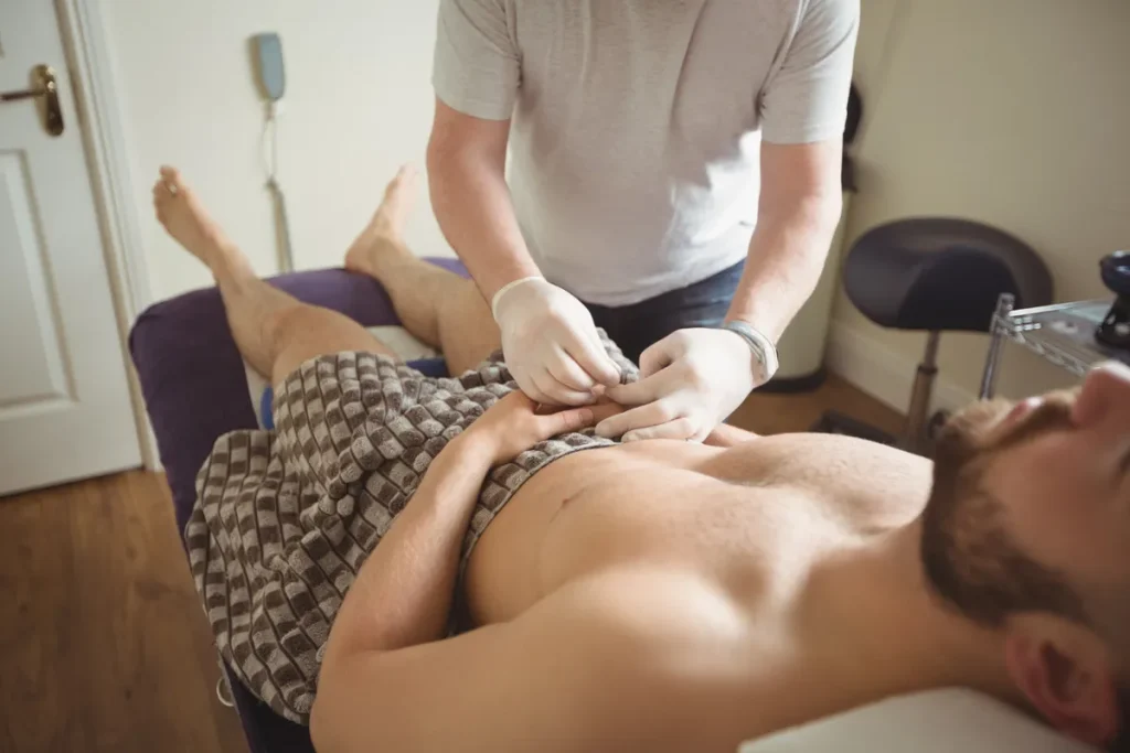 Terapeuta realizando massagem redutora ou modeladora na região abdominal de um homem deitado em maca.