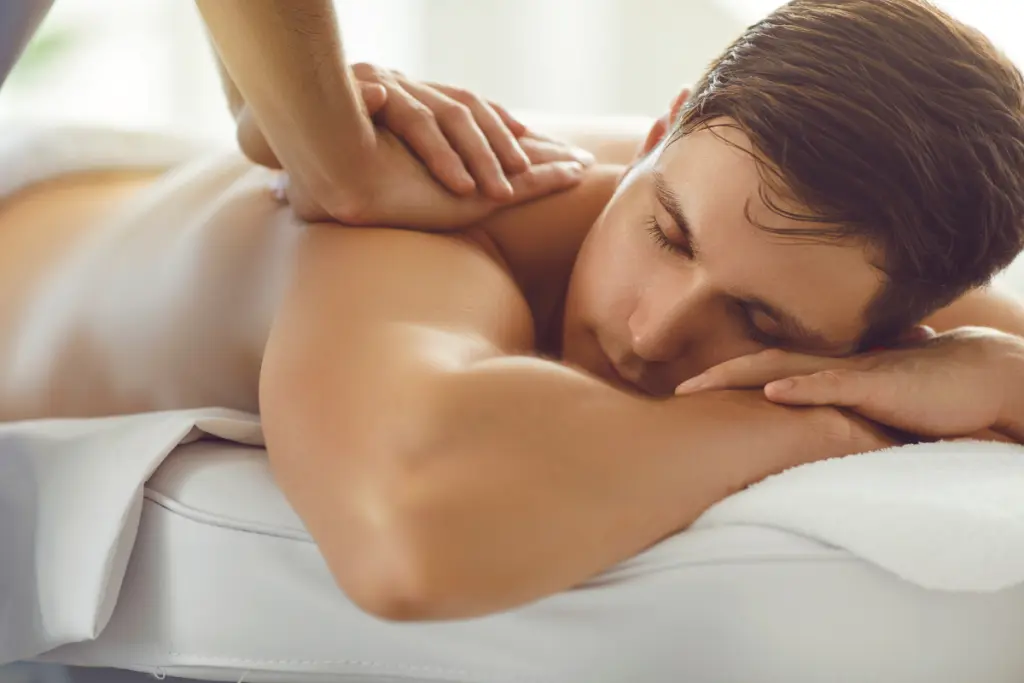 Homem recebendo massagem relaxante nas costas em uma maca de spa, com expressão tranquila e ambiente iluminado suavemente.