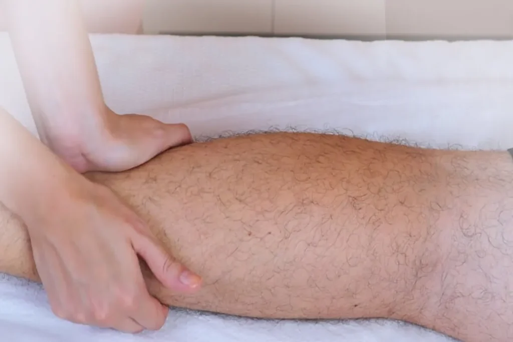 Close-up das mãos de um terapeuta aplicando massagem ou terapia manual na panturrilha de um paciente, focado no alívio de dor muscular.