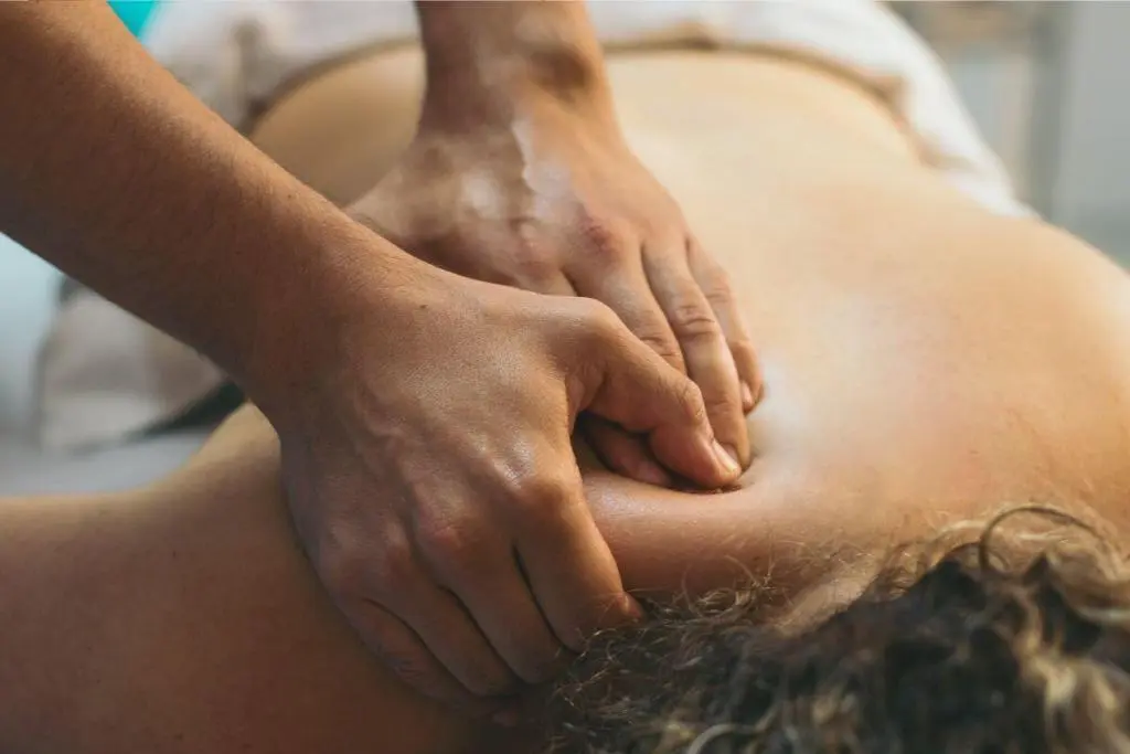 Mãos de terapeuta aplicam massagem terapêutica nas costas de um homem durante sessão de relaxamento corporal