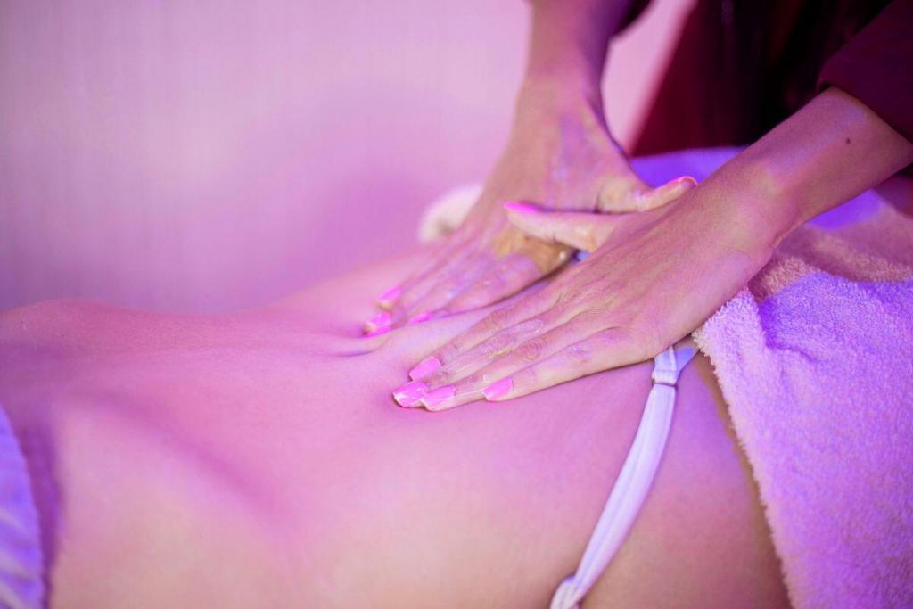 Mãos aplicando massagem com óleo na lombar de uma pessoa deitada em ambiente com luz suave.