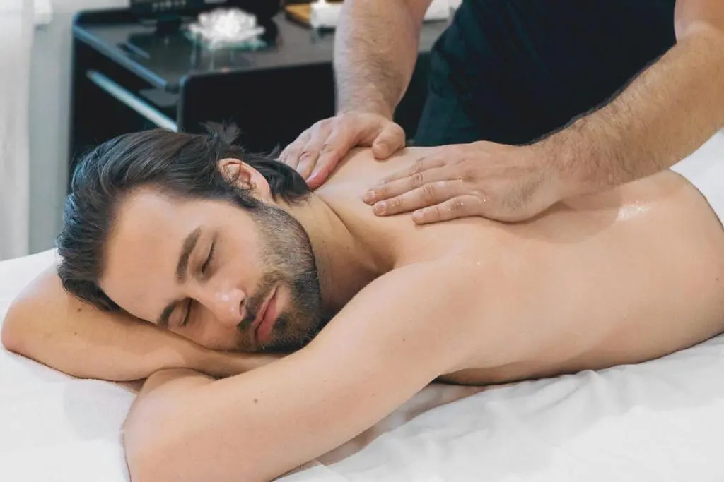 Homem recebendo massagem relaxante nas costas, deitado com os olhos fechados enquanto o massoterapeuta aplica técnica manual.