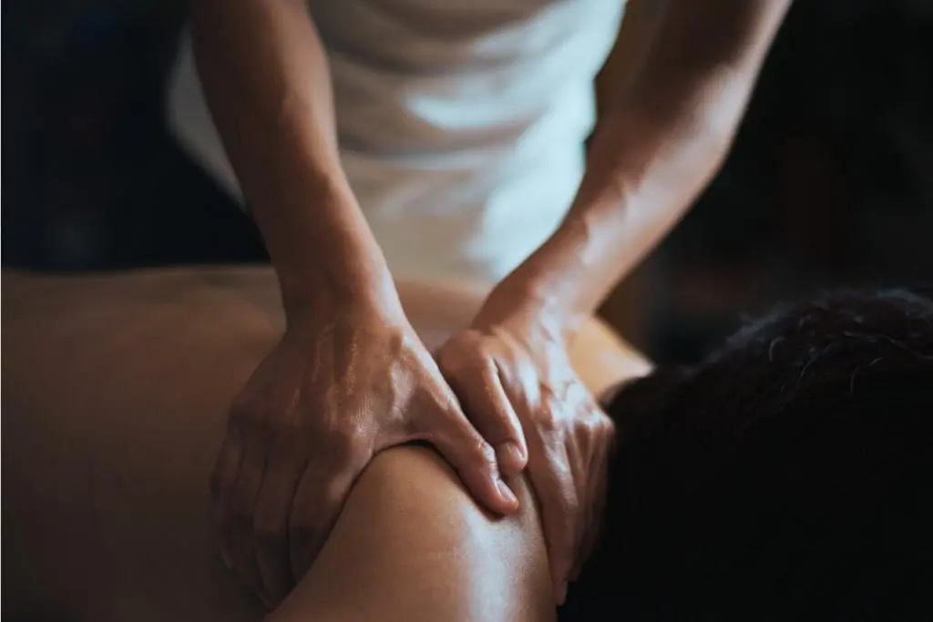Terapeuta realizando massagem relaxante nas costas de uma pessoa deitada, com foco nas mãos aplicando pressão suave em ambiente tranquilo.