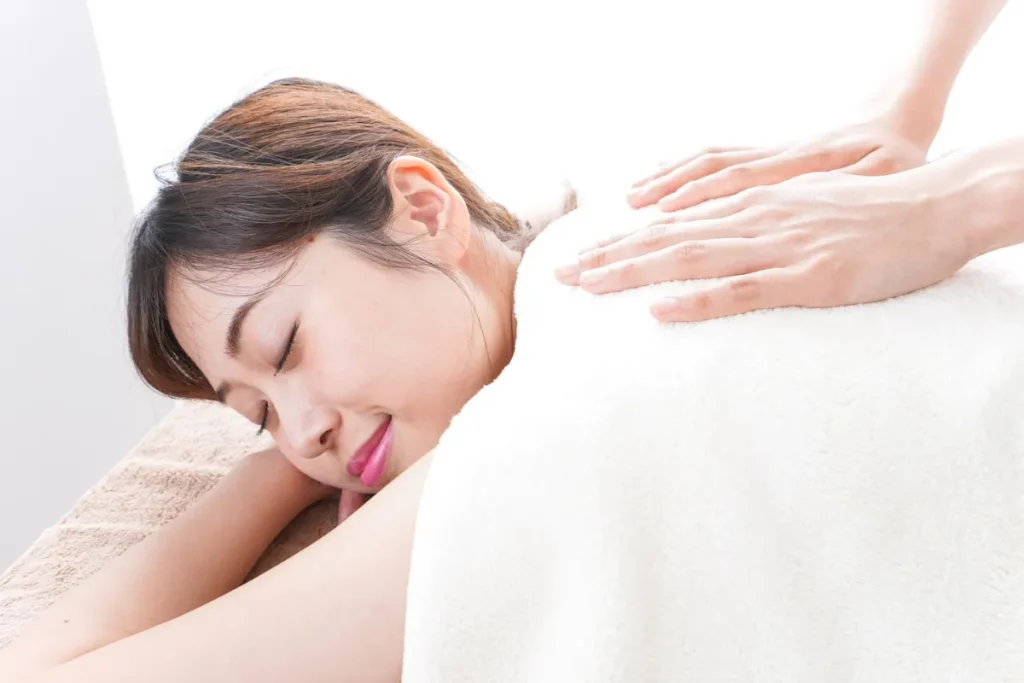 Mulher deitada de olhos fechados enquanto recebe massagem nas costas em ambiente claro.