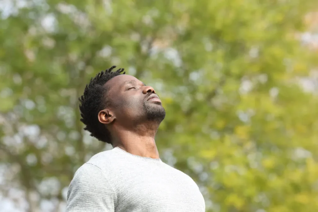 Homem com olhos fechados respirando profundamente ao ar livre em meio à natureza.