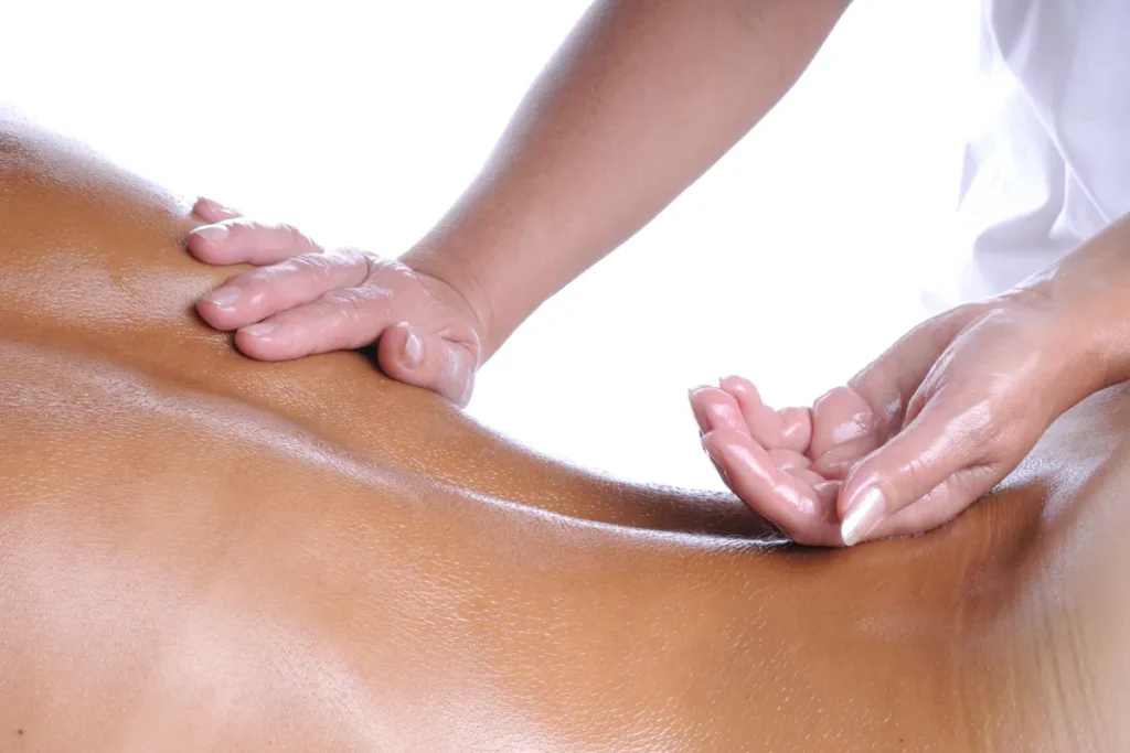 mãos aplicando óleo nas costas de uma pessoa durante massagem com iluminação clara