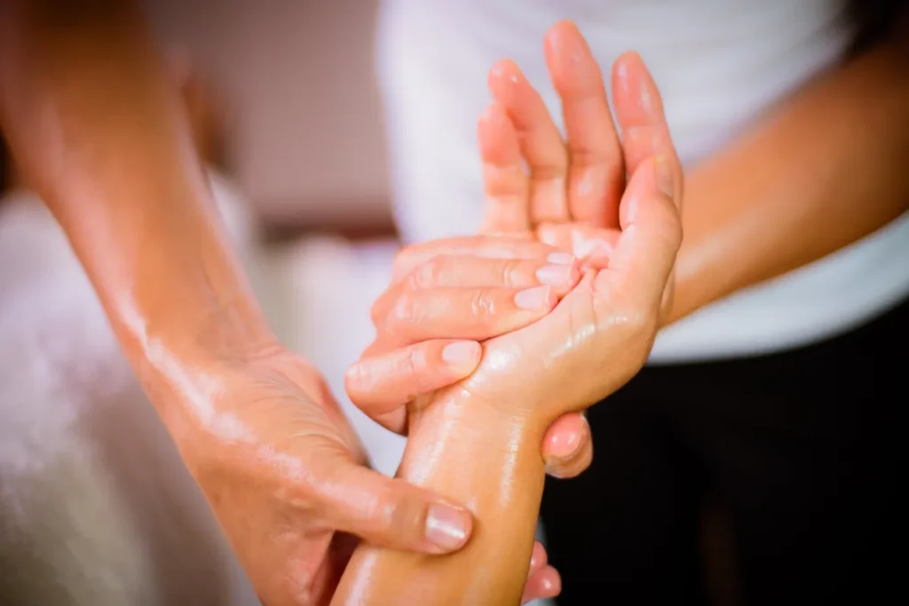 mãos realizando massagem no punho de uma pessoa com uso de óleo