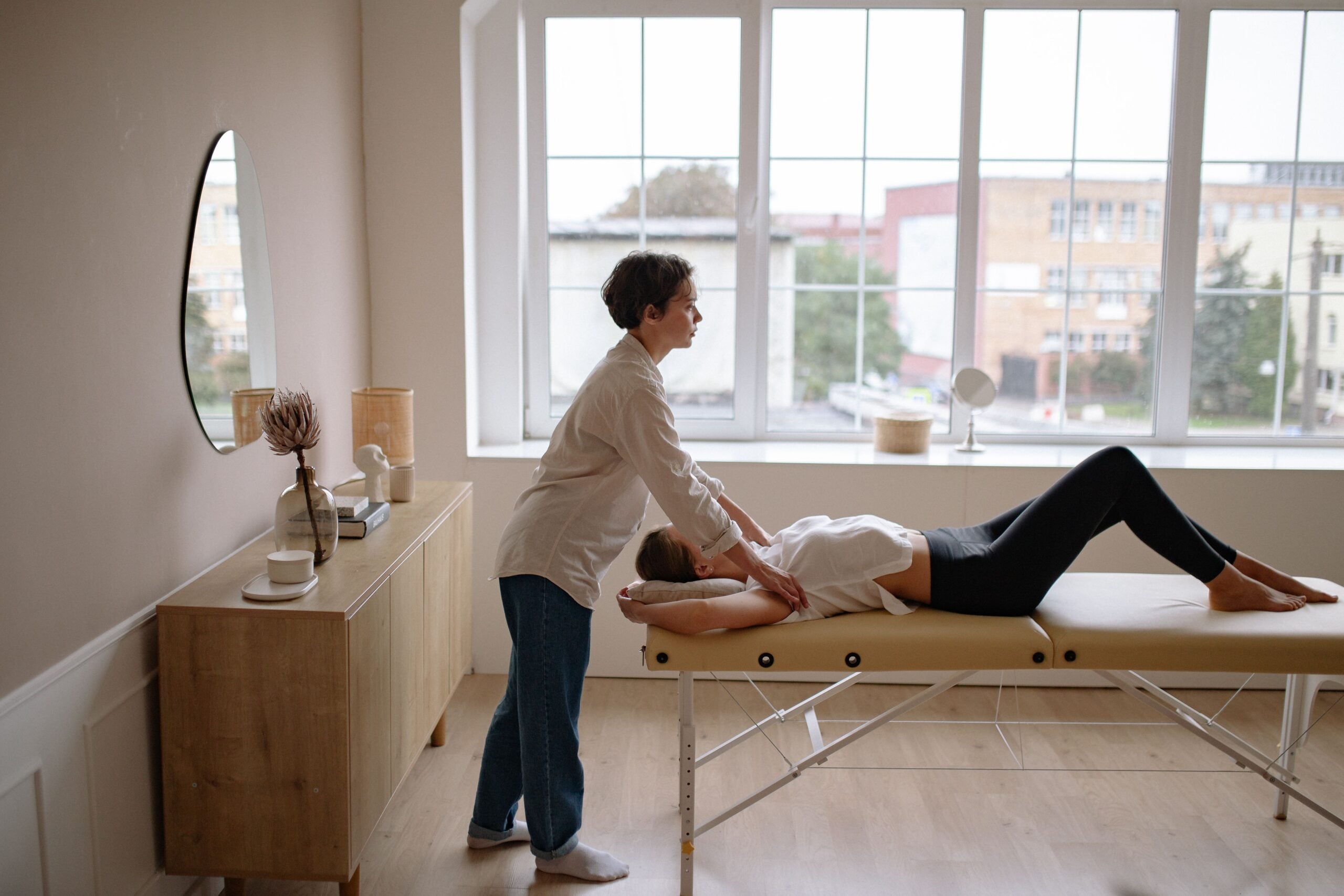 Profissional realizando massagem em uma pessoa deitada sobre maca em ambiente claro e organizado