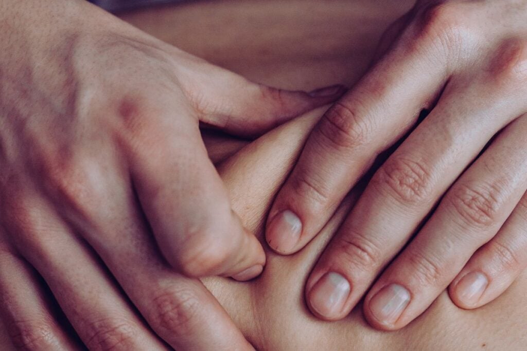 Close das mãos de um profissional aplicando pressão manual durante sessão de massagem terapêutica.