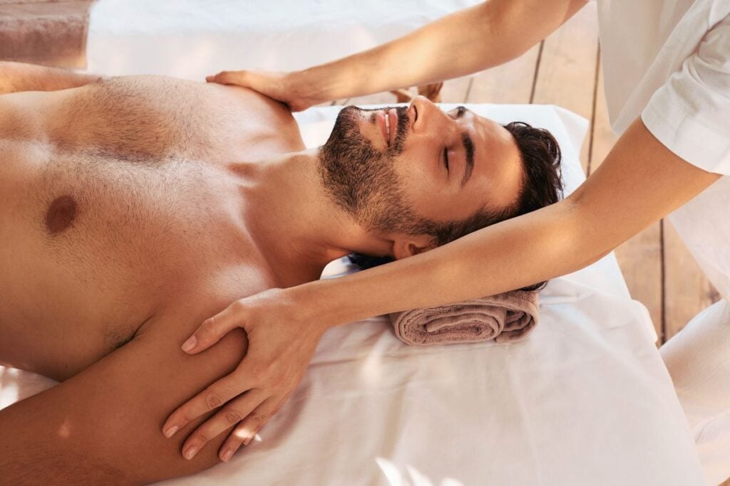 Homem recebendo massagem sensitiva nos ombros e braços em ambiente tranquilo de relaxamento.