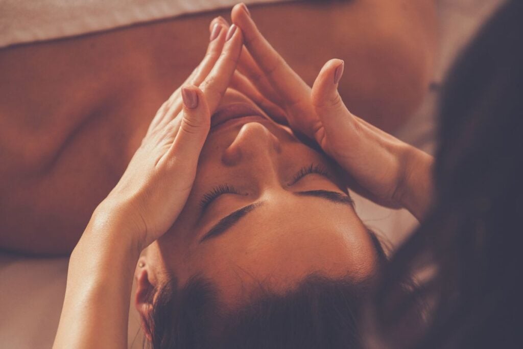 Pessoa recebendo massagem facial com movimentos suaves na testa e na região dos olhos.